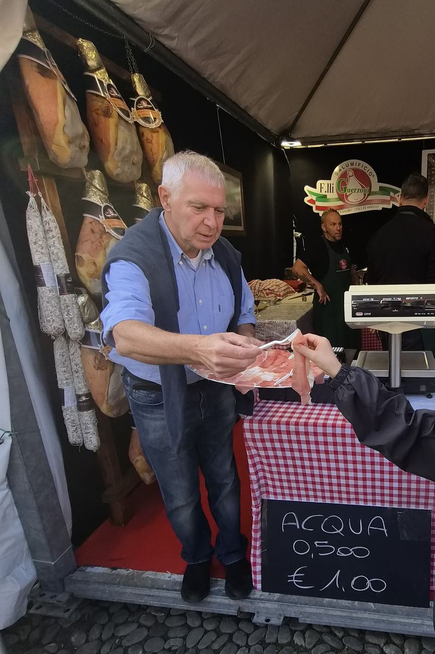 A butcher from Salumificio F.lli Guerzoni holding out a plate of Prosciutto di Modena