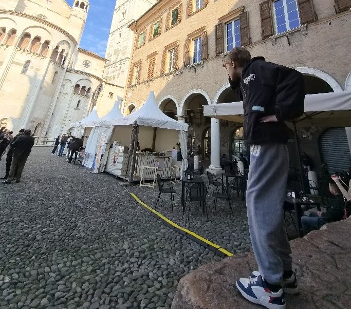 Jemand steht auf der Preda Ringadora auf der Piazza Grande in Modena, dahinter der Dom und die Ghirlandina